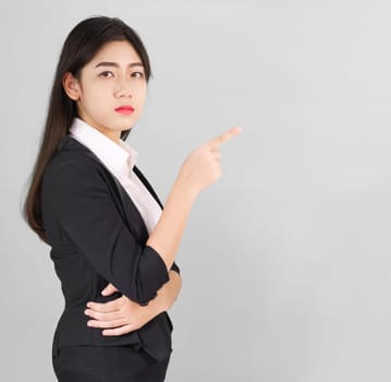 Asian woman in suit looking at camera and pointing finger on gray background