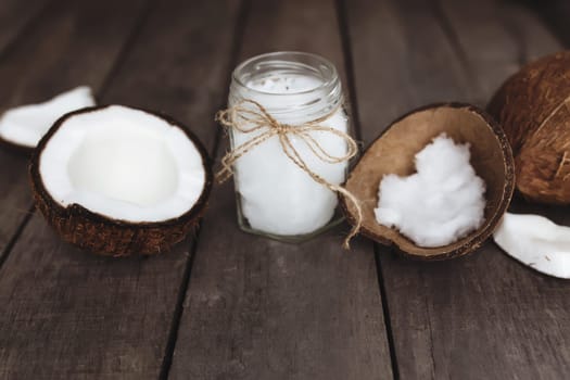 Broken coconuts on gray wooden background with jar of raw organic extra virgin coconut oil. White coconut pulp. High quality photo