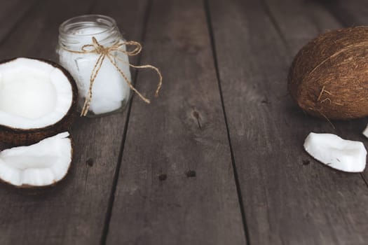 Broken coconuts on gray wooden background with jar of raw organic extra virgin coconut oil. White coconut pulp. High quality photo