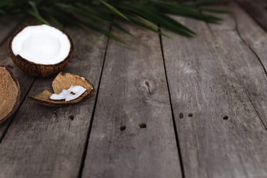 Broken coconuts on gray wooden background with palm leaf. White coconut pulp. High quality photo