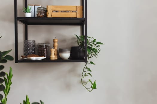 Black metal shelves in the kitchen on a gray concrete wall in a loft style. Green flowerpots. High quality photo