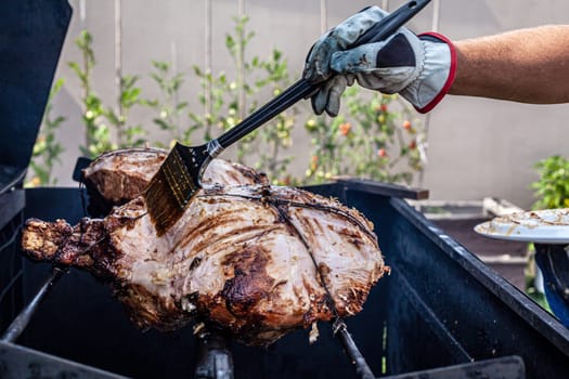 Man hand grilling barbecue with big pork at backyard on day. Family dinner outdoor style bbq activity.