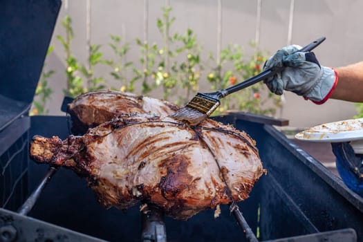 Man hand grilling barbecue with big pork at backyard on day. Family dinner outdoor style bbq activity.