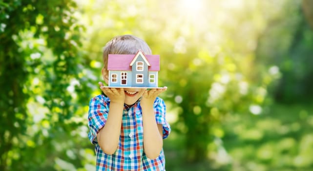 Little child holding in his hands model of the blue wooden house. Concept of the selling, buying and renting of the house.