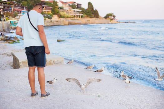 A young guy is feeding a flock of seagulls. Sun, summer, sea.