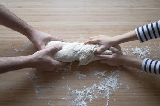 side view close up portrait of Caucasian child hands working the dough at home with his father on a kitchen wood cutting board in natural window light