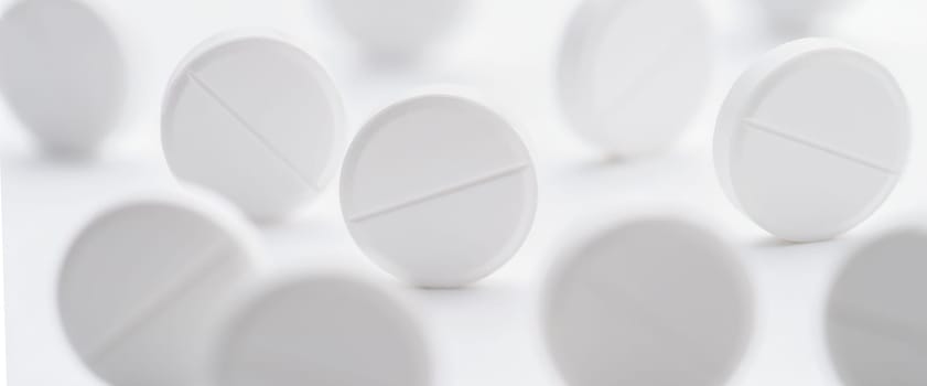 A pile of white pills scattered on a bright white background. Selective focus. Mockup layout, template.