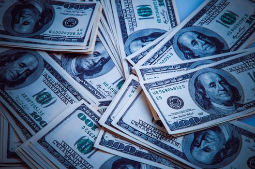 Cash of hundred dollar bills, dollar background image. One hundred US banknotes are scattered over the background. Style blue color and vignetting.