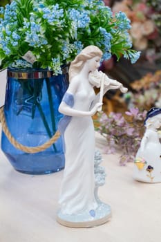 German porcelain figurine of a violinist girl. Ceramic figurine of the violoncellist in retro style with blue flowers in a vase on the table