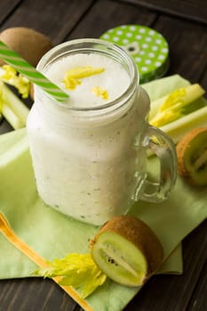 Blended green smoothie with ingredients celery and kiwi on wooden table, vertical image