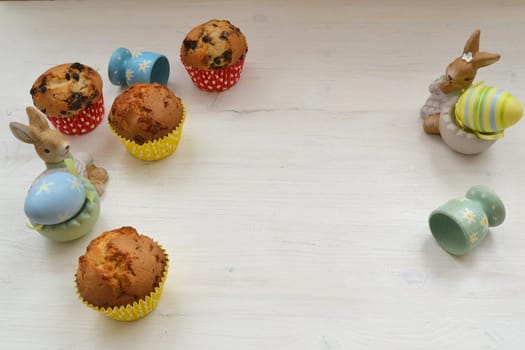 Easter table with muffins, colored eggs and bunnies. Copy space, white table