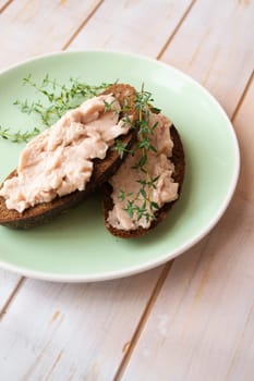 Homemade meat snack chicken liver pate with savory and olives on slices of dark bread. Vertical image