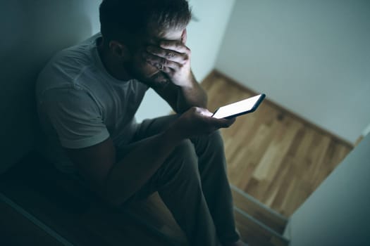 Depressed man sitting in the dark with his smartphone
