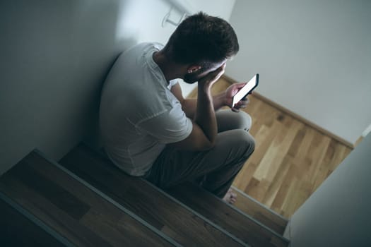 Depressed man sitting in the dark with his smartphone