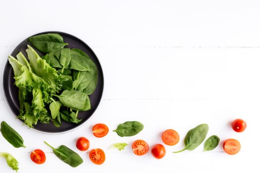Flat lay with bowl of fresh green salad leaves, lettuce, spinach and red cherry tomatoes cups and halves on a white background. Healthy vegetarian eating concept. High quality photo