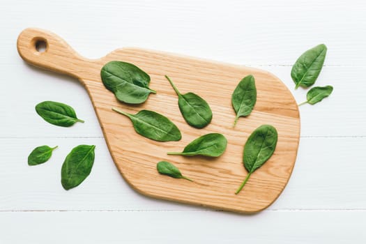 Wooden cutting board with fresh green salad leaves of spinach on white background. Healthy vegetarian eating concept. High quality photo