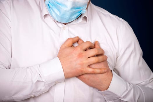 Man wearing medical face mask with chest pain - heart attack, shortness of breath during work in office.