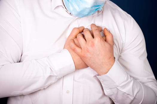 Man wearing medical face mask with chest pain - heart attack, shortness of breath during work in office.