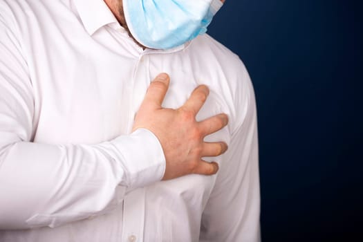 Man wearing medical face mask with chest pain - heart attack, shortness of breath during work in office.