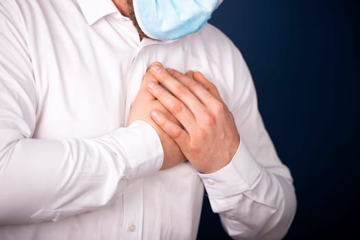 Man wearing medical face mask with chest pain - heart attack, shortness of breath during work in office.