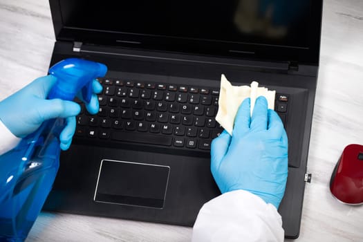 Office sanitizing wiping laptop with disinfectant. Coronavirus COVID-19 sanitize cleaning, disinfection of work desk.