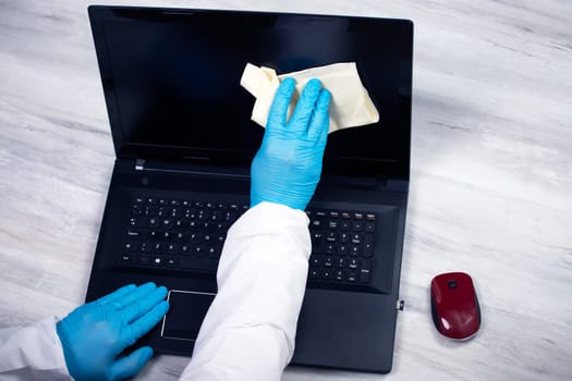 Office sanitizing wiping laptop with disinfectant. Coronavirus COVID-19 sanitize cleaning, disinfection of work desk.