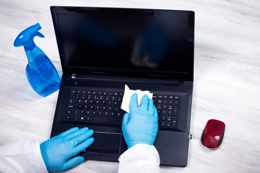 Office sanitizing wiping laptop with disinfectant. Coronavirus COVID-19 sanitize cleaning, disinfection of work desk.
