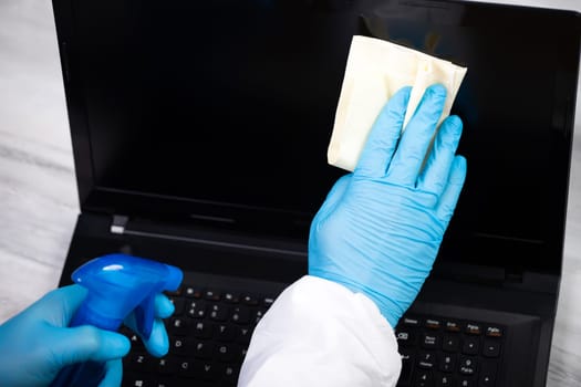 Office sanitizing wiping laptop with disinfectant. Coronavirus COVID-19 sanitize cleaning, disinfection of work desk.