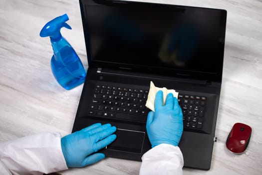 Office sanitizing wiping laptop with disinfectant. Coronavirus COVID-19 sanitize cleaning, disinfection of work desk.