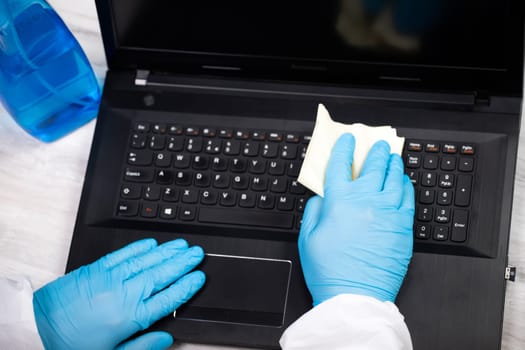 Office sanitizing wiping laptop with disinfectant. Coronavirus COVID-19 sanitize cleaning, disinfection of work desk.