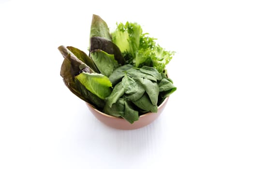 Flat lay with bowl of fresh green salad leaves of spinach and lettuce, romaine and basil on white background. Healthy vegetarian eating concept. High quality photo