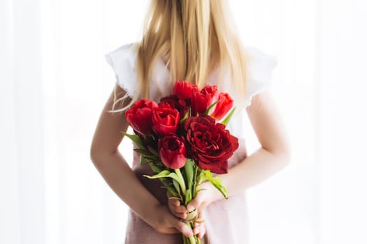 Small girl holding bouquet of red tulip flowers. Concept for greeting card for Easter, Mother's day, International women's day, Saint Valentine's day. High quality photo