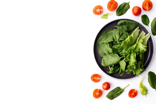 Flat lay with bowl of fresh green salad leaves, lettuce, spinach and red cherry tomatoes cups and halves on a white background. Healthy vegetarian eating concept. High quality photo