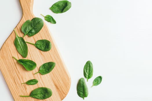 Wooden cutting board with fresh green salad leaves of spinach on white background. Healthy vegetarian eating concept. High quality photo