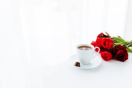 Red tulips bouquete on table, white coffee cup. Concept for greeting card for mothers day, international womans day or valentines day concept, birthday greeting concept, dark chocolate candy