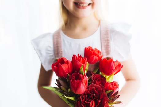 Small smiling girl holding bouquet of red tulip flowers. Concept for greeting card for Easter, Mother's day, International women's day, Saint Valentine's day. High quality photo