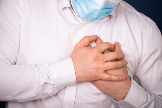 Man wearing medical face mask with chest pain - heart attack, shortness of breath during work in office.