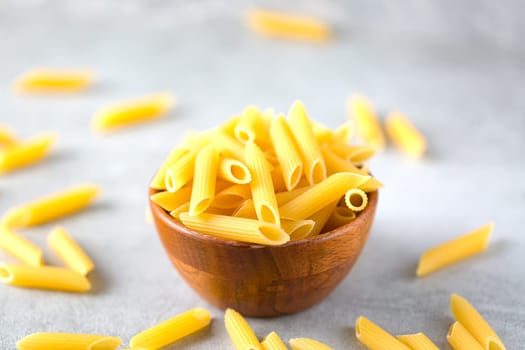 Uncooked yellow pasta in a wooden bowl on gray table. Selective focus. Italian food concept. Copy space. World Pasta Day.