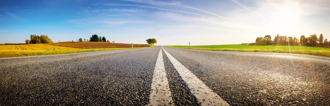 Wide asphalt road panorama in countryside on summer day. Route with white dividing lines in beautiful nature landscape.