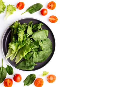 Flat lay with bowl of fresh green salad leaves, lettuce, spinach and red cherry tomatoes cups and halves on a white background. Healthy vegetarian eating concept. High quality photo