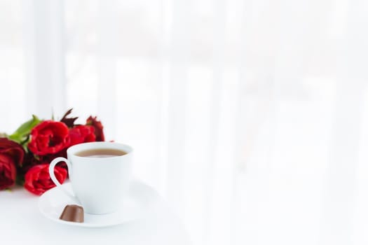 Red tulips bouquete on table, white coffee cup. Concept for greeting card for mothers day, international womans day or valentines day concept, birthday greeting concept, dark chocolate candy