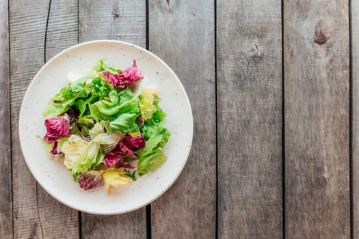 Healthy eating concept flat lay. Plate with mix of fresh green salad leaves, lettuce radicchio, basil on wooden background. Healthy eating concept. Vegetarian concept. Vegan food. Gardening concept.
