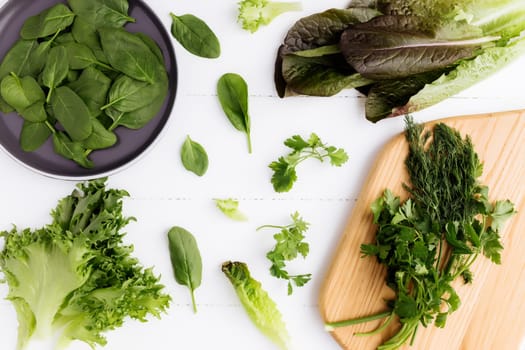 Flat lay with cutting board and bowl of fresh green salad leaves of spinach and lettuce, romaine and parsley, basil on white background. Healthy vegetarian eating concept. High quality photo