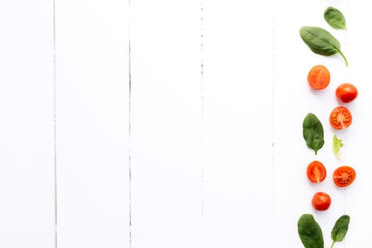 Flat lay with red cherry tomatoes and green spinach leaves on a white wooden background. Healthy eating concept. High quality photo