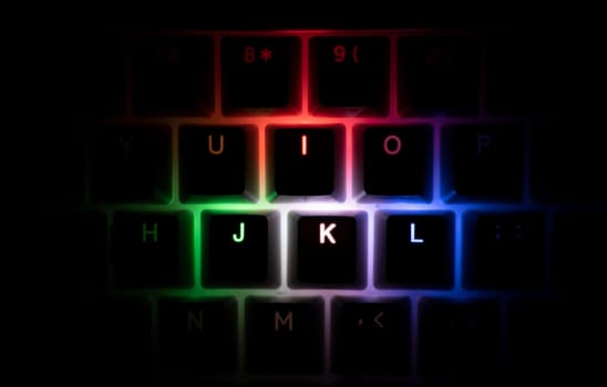 top view detail closeup of illuminated RGB keycaps keys on black on black gaming keyboard shining in different colors in the dark