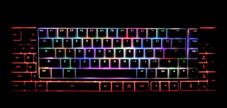 top view detail closeup of two illuminated mechanical gaming RGB keyboard on black desk on top of each other with keycaps lighting up in different colors in the dark