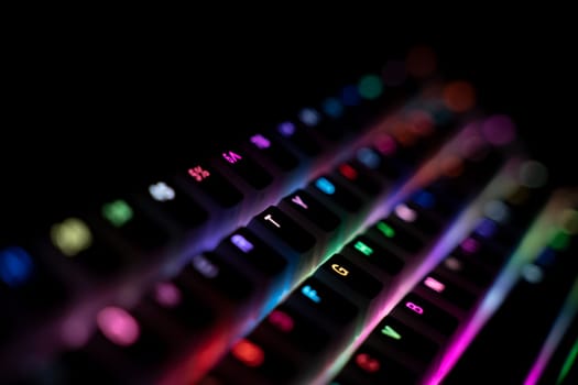 perspective side view detail closeup with shallow depth of field of illuminated mechanical gaming RGB keyboard with keycaps lighting up in different colors in the dark