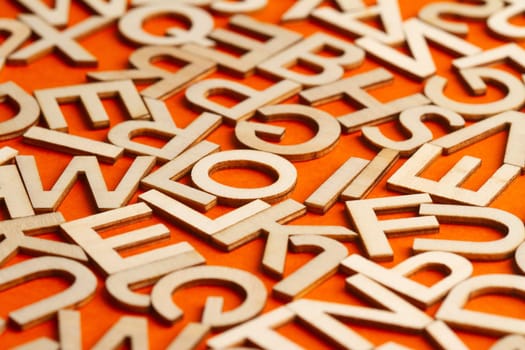 perspective view closeup detail macro of many wooden cut small alphabet letters on orange background