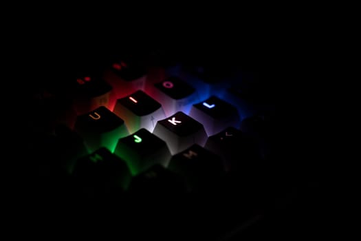 side view detail closeup of illuminated RGB keycaps keys on black on black gaming keyboard shining in different colors in the dark