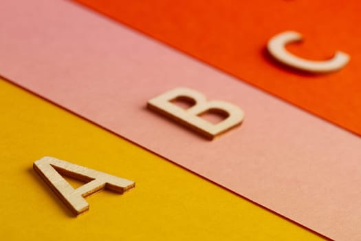 side view perspective closeup of A B and C letters of the alphabet cut in wood on colored paper background